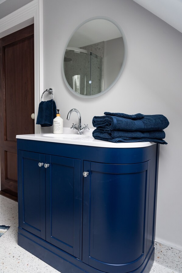A bathroom with a dark blue vanity, a white sink, a round mirror, and a towel stacked on the sink.