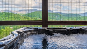 A hot tub with a view of green hills and mountains through a wooden fence. - Private Indoor Pool, Hot Tub, Free Attractions, Pool Table, Fire Pit (Gatlinburg)
