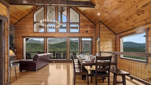 A spacious wooden interior with a dining area, a sofa, and large windows offering mountain views. - Private Indoor Pool, Hot Tub, Free Attractions, Pool Table, Fire Pit (Gatlinburg)