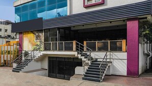A building with a modern facade, a staircase leading to an upper level, and a covered outdoor area with railings. - Classic HBR Layout Formerly Leela Park (Bengaluru)