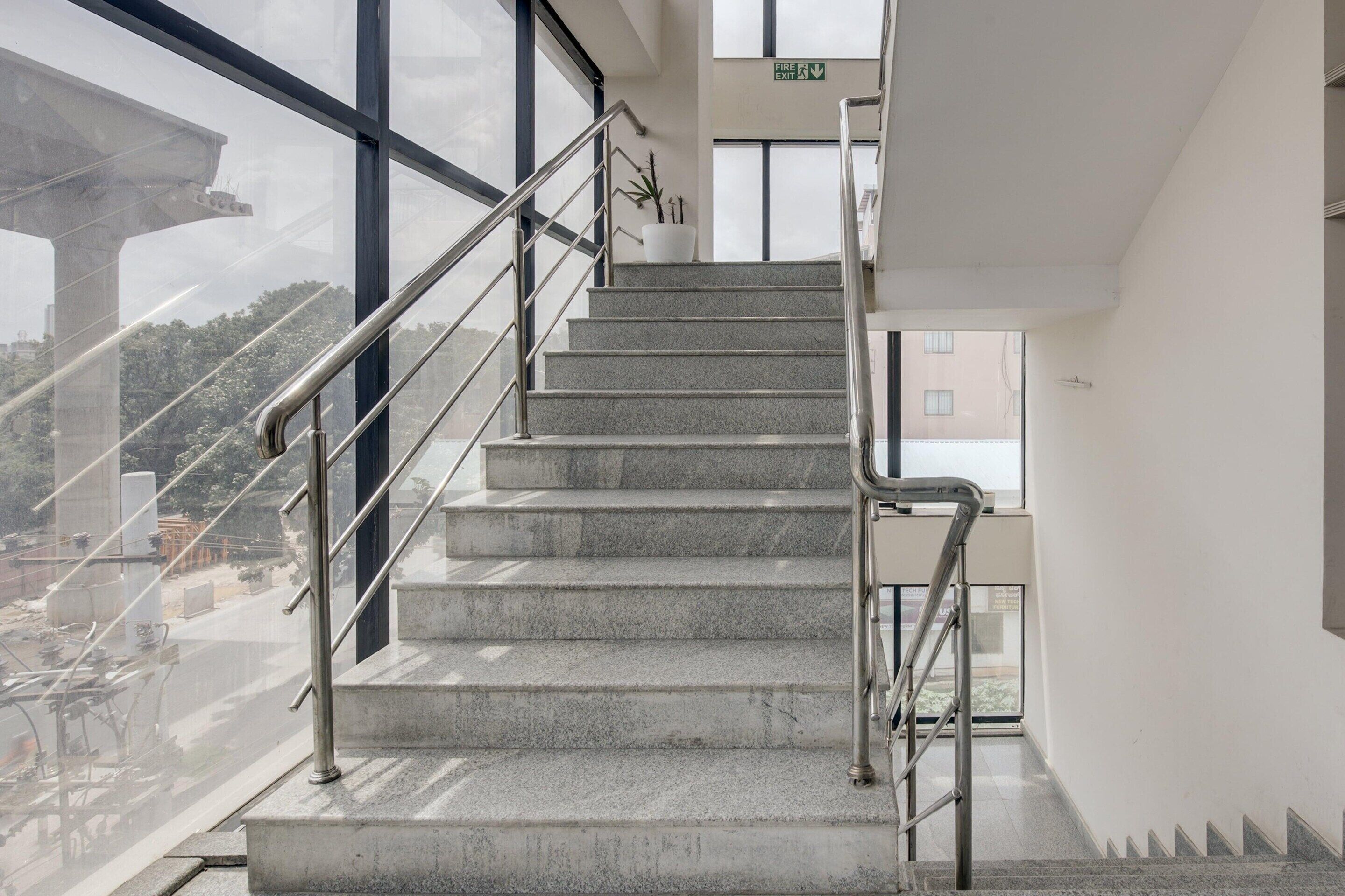 A staircase with metal railings leading to an exit, large windows, and a view of the outside.