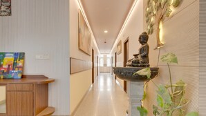 A hallway with a statue, a desk with a colorful painting, and a plant. - Classic HBR Layout Formerly Leela Park (Bengaluru)