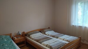 A bedroom with a wooden bed, a bedside table with a lamp, and a window with sheer curtains. - Lavender Apartment (Siófok)