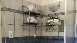 A small bathroom with a blue sink, a towel rack with towels, a mirror, and a shower area. - Lavender Apartment (Siófok)