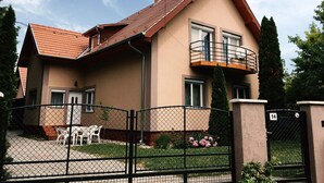 A two-story house with a red-tiled roof, a balcony on the upper floor, and a fenced front yard with a table and chairs. - Lavender Apartment (Siófok)