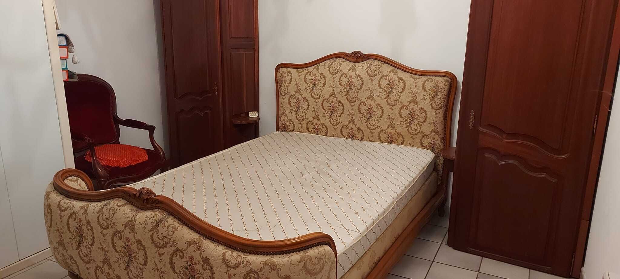Quarto com cama de madeira, uma cadeira vermelha e um guarda-roupa.