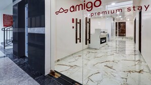 En modern hotellobby med ett marmorgolv, en glasvägg med logotypen för ”Amigo Premium Stay” och en receptionsdisk.