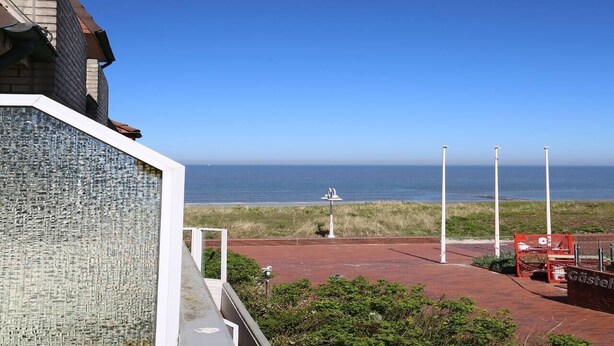 Une vue sur la côte, avec un ciel dégagé, une statue et un chemin de briques rouges menant à la plage.