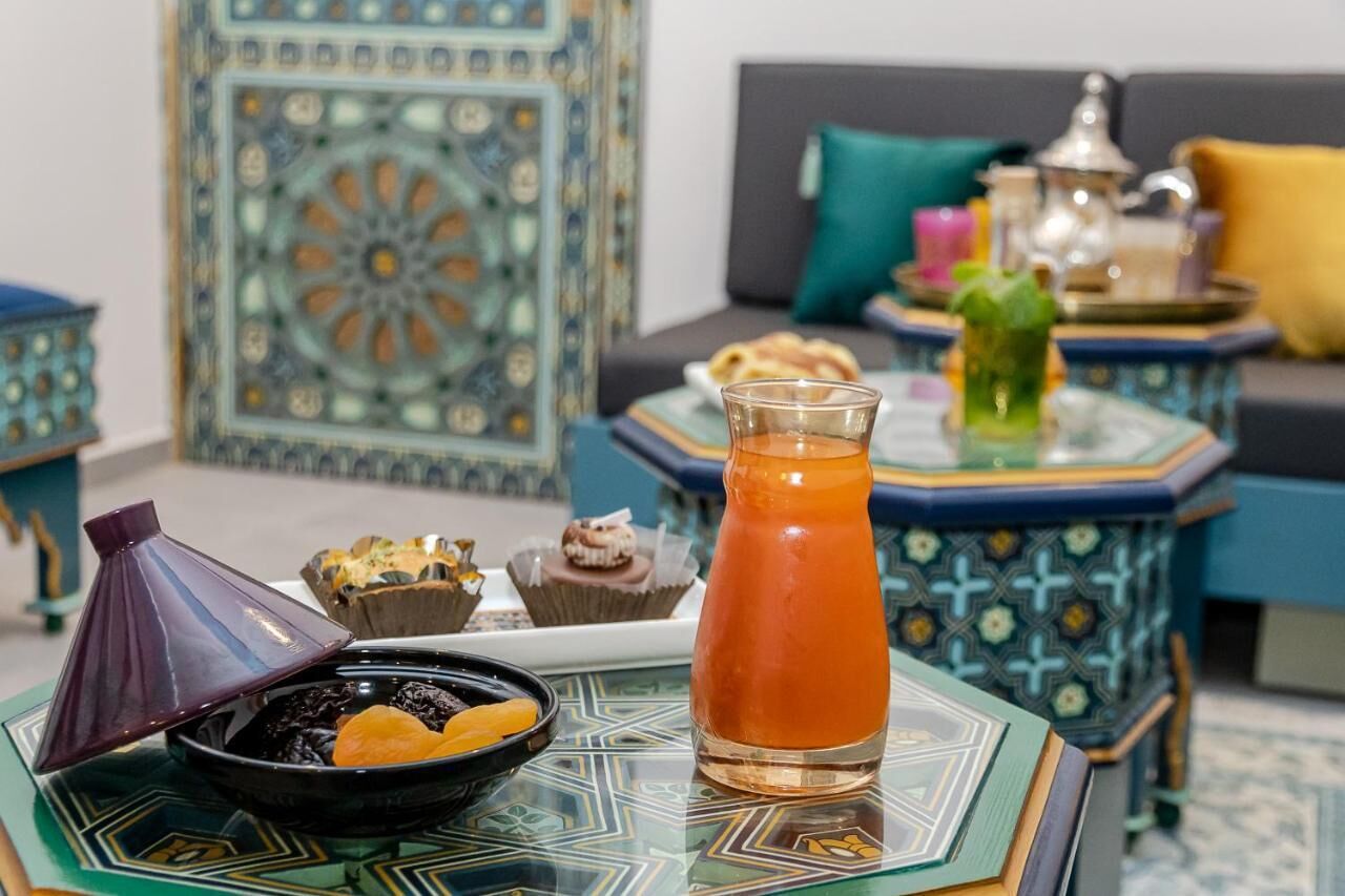 A dining area with a table set for a meal, including a pitcher of tea, a bowl of dates, and pastries.