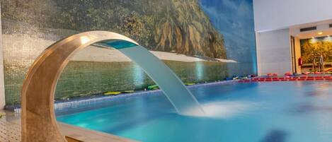 A swimming pool with a waterfall feature, a mural of a tropical landscape, and a red poolside area.