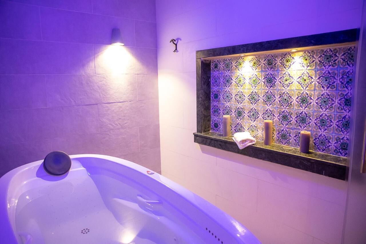 A bathroom with a bathtub, a tiled wall with a decorative pattern, and a shelf with candles.