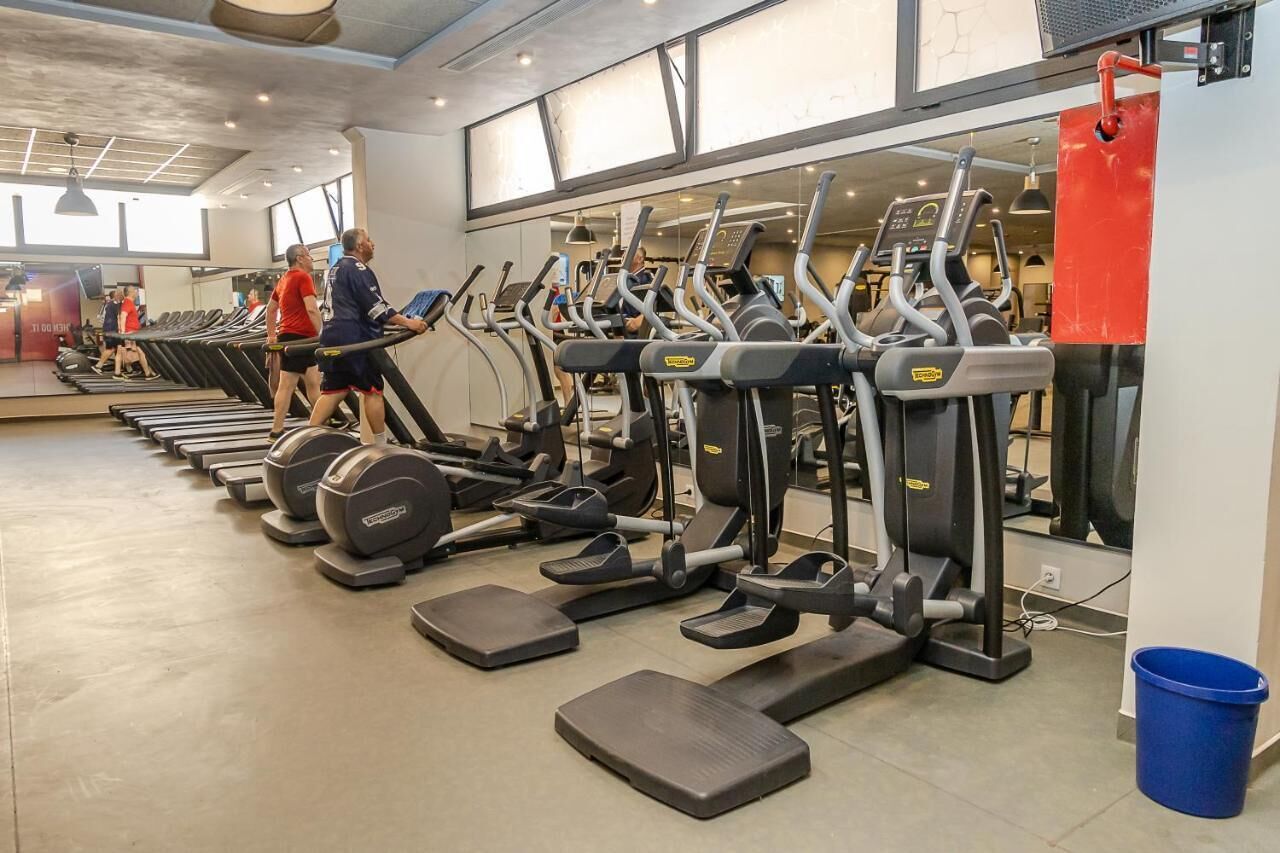 A gym with multiple treadmills and elliptical machines arranged in rows.