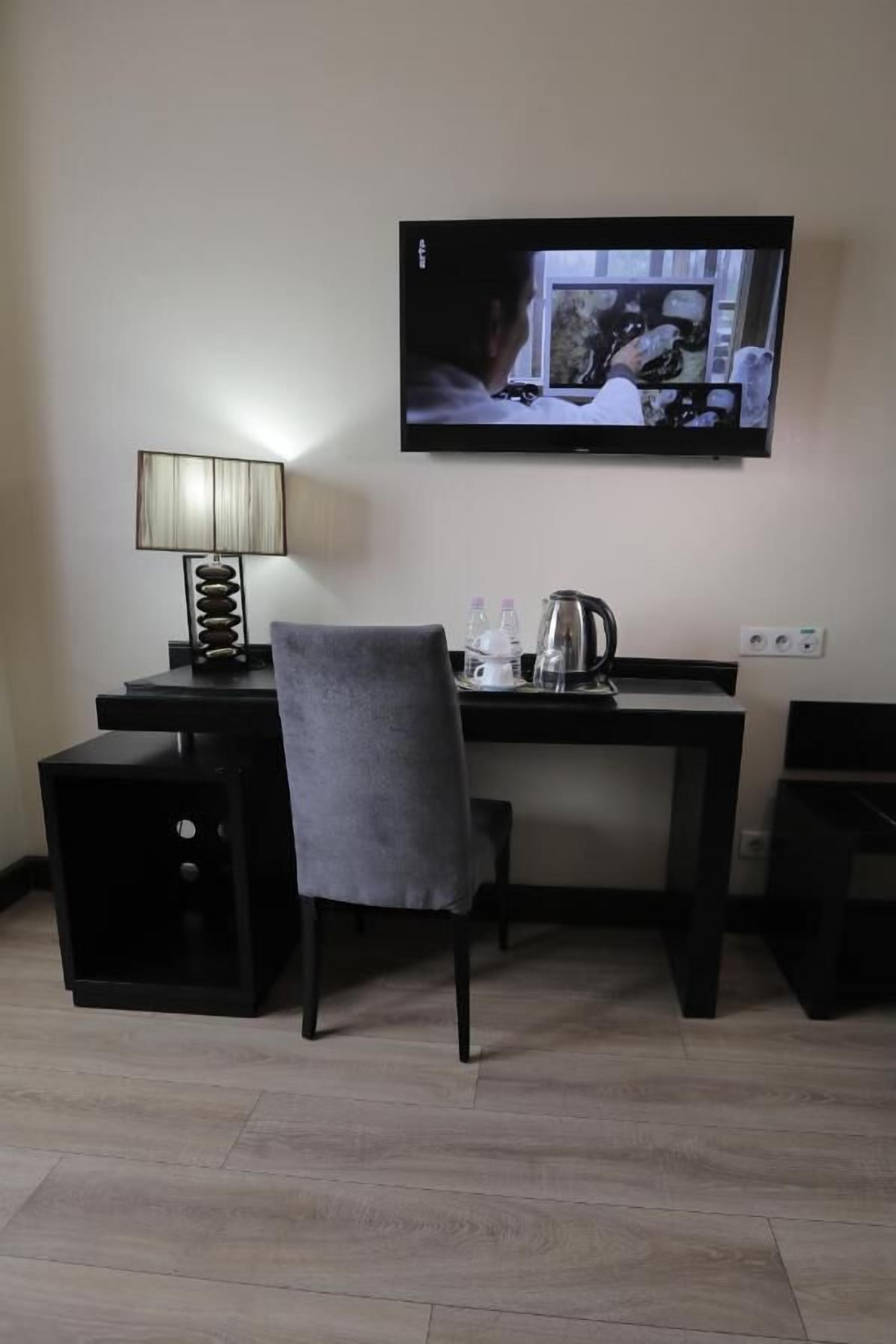 Une chambre d’hôtel équipée d’un bureau, d’une chaise, d’une lampe et d’un téléviseur diffusant une scène.