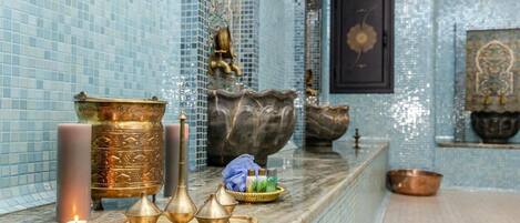 A bathroom with a blue mosaic wall, a mirror, and a decorative brass basin on the counter.