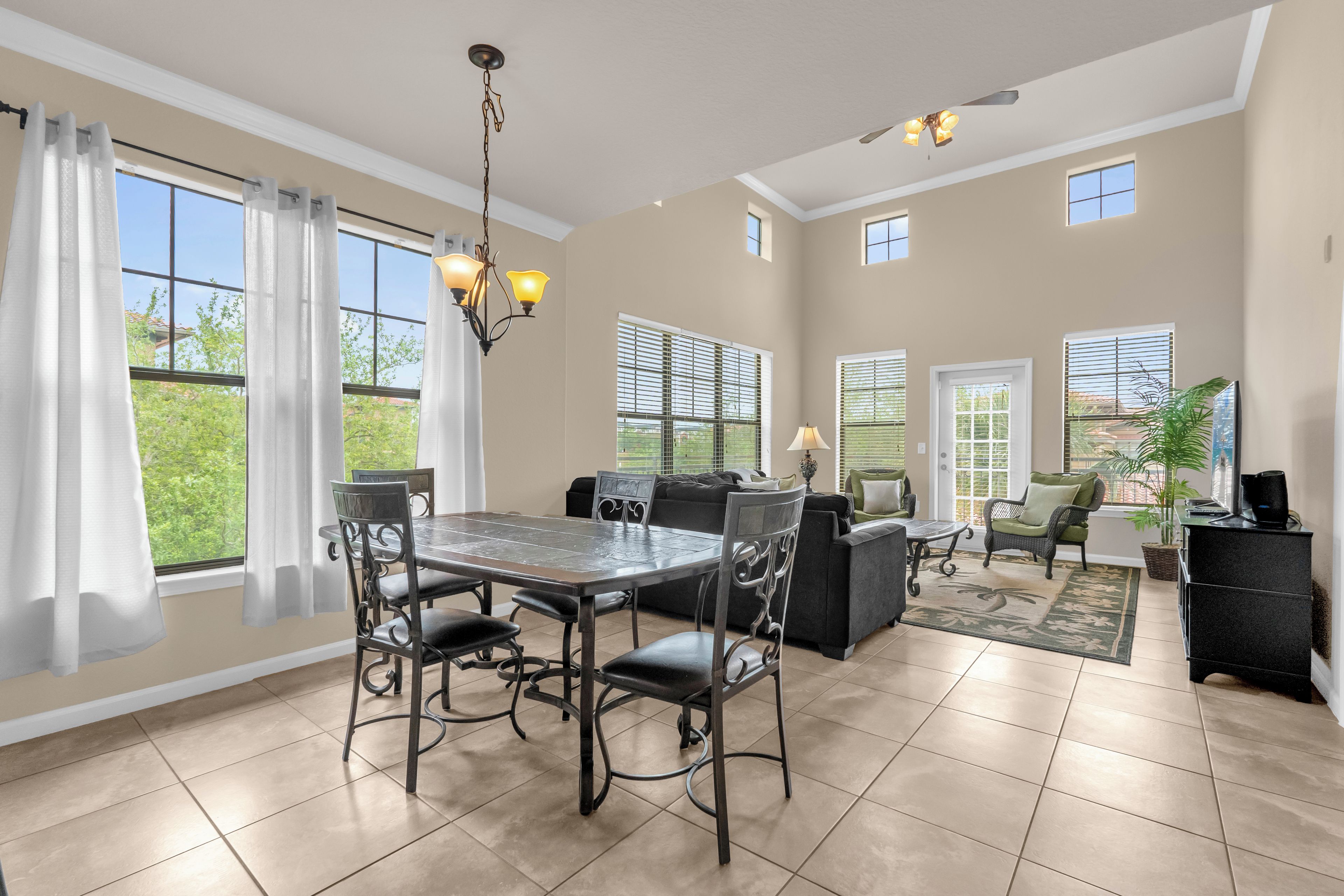 A spacious living room with a dining area, large windows, and a ceiling fan.