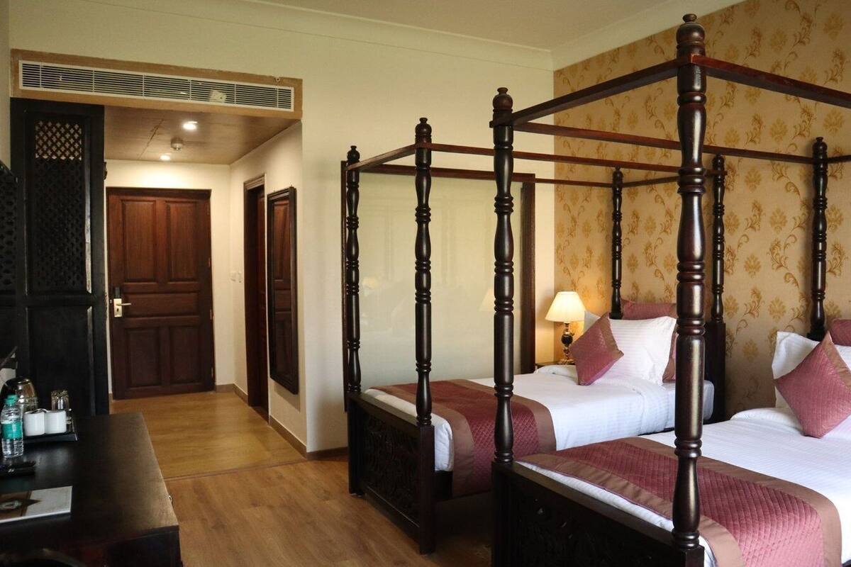 Uma cama de dossel com duas camas num quarto com soalho de madeira e papel de parede estampado.