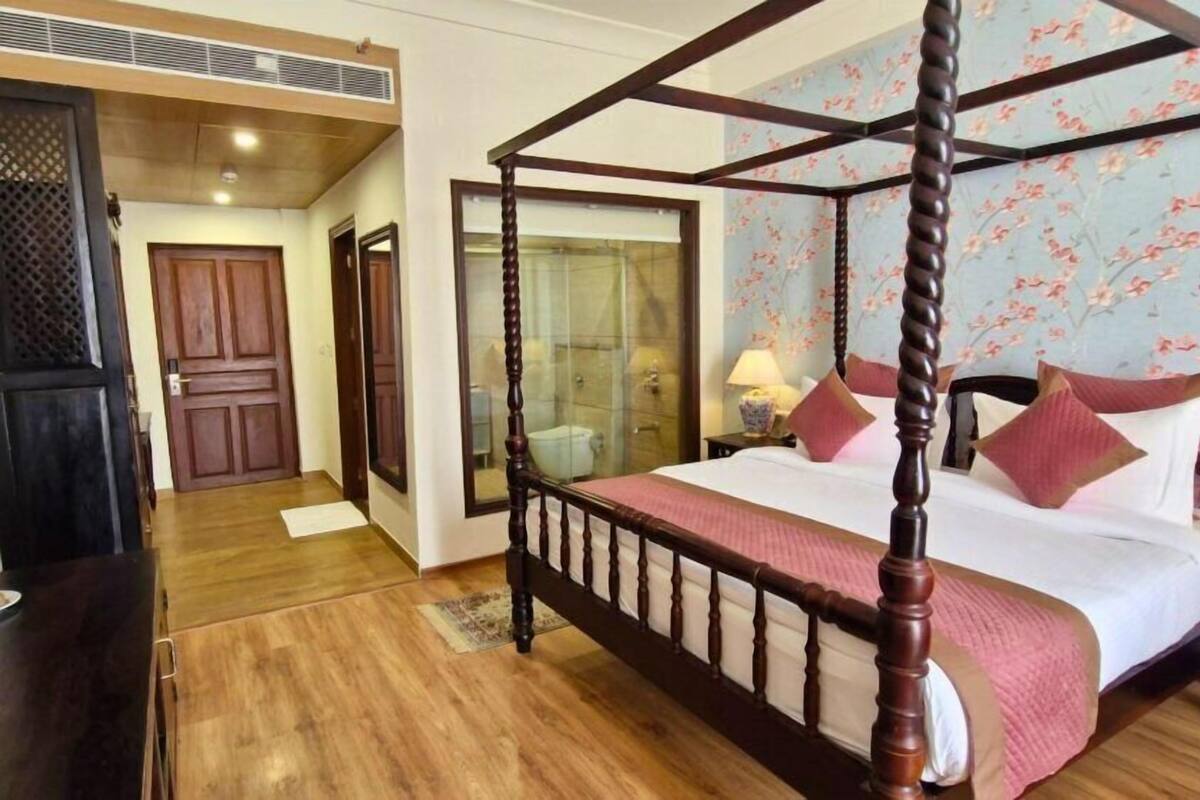 Uma cama com dossel e estrutura de madeira, banheiro com paredes de vidro e papel de parede floral.