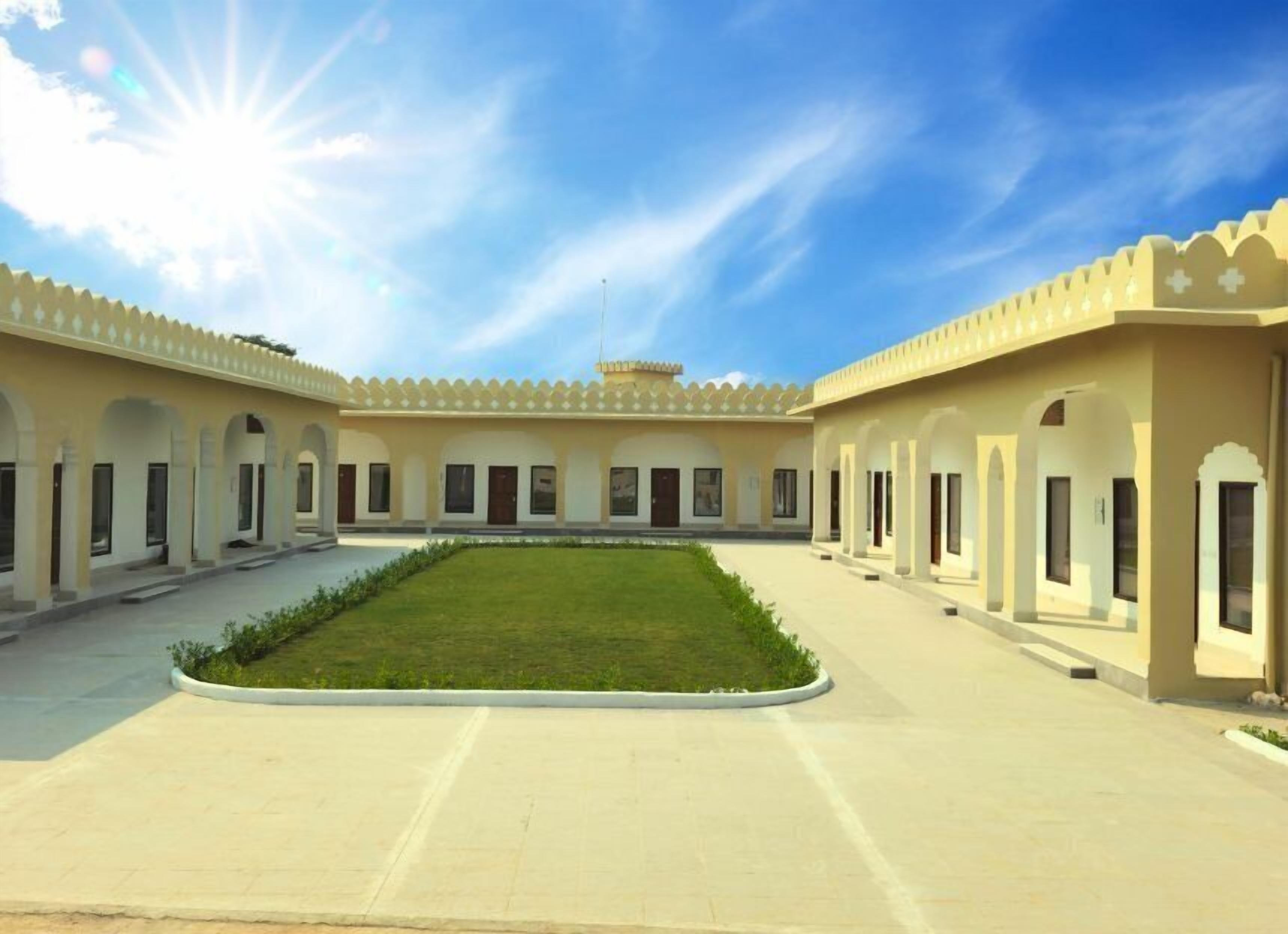 A courtyard with a central lawn, surrounded by buildings with arched doorways and windows.