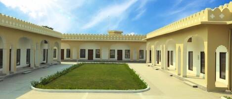 A courtyard with a central lawn, surrounded by buildings with arched doorways and windows.