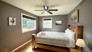 Ein Schlafzimmer mit einem Bett, einem Deckenventilator, einem Fenster und einem Nachttisch mit einer Lampe.