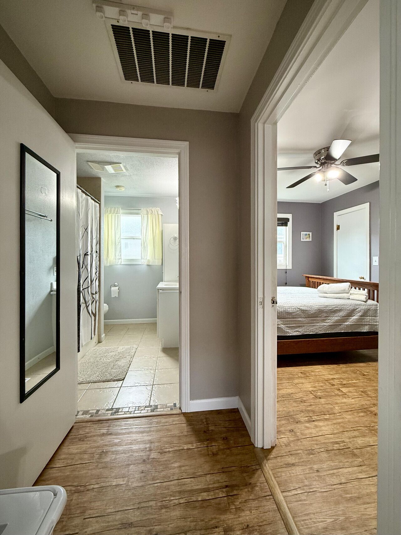Un dormitorio con piso de madera, ventilador de techo y cama con ropa de cama blanca.