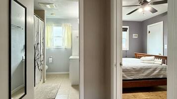 Un dormitorio con piso de madera, ventilador de techo y cama con ropa de cama blanca.