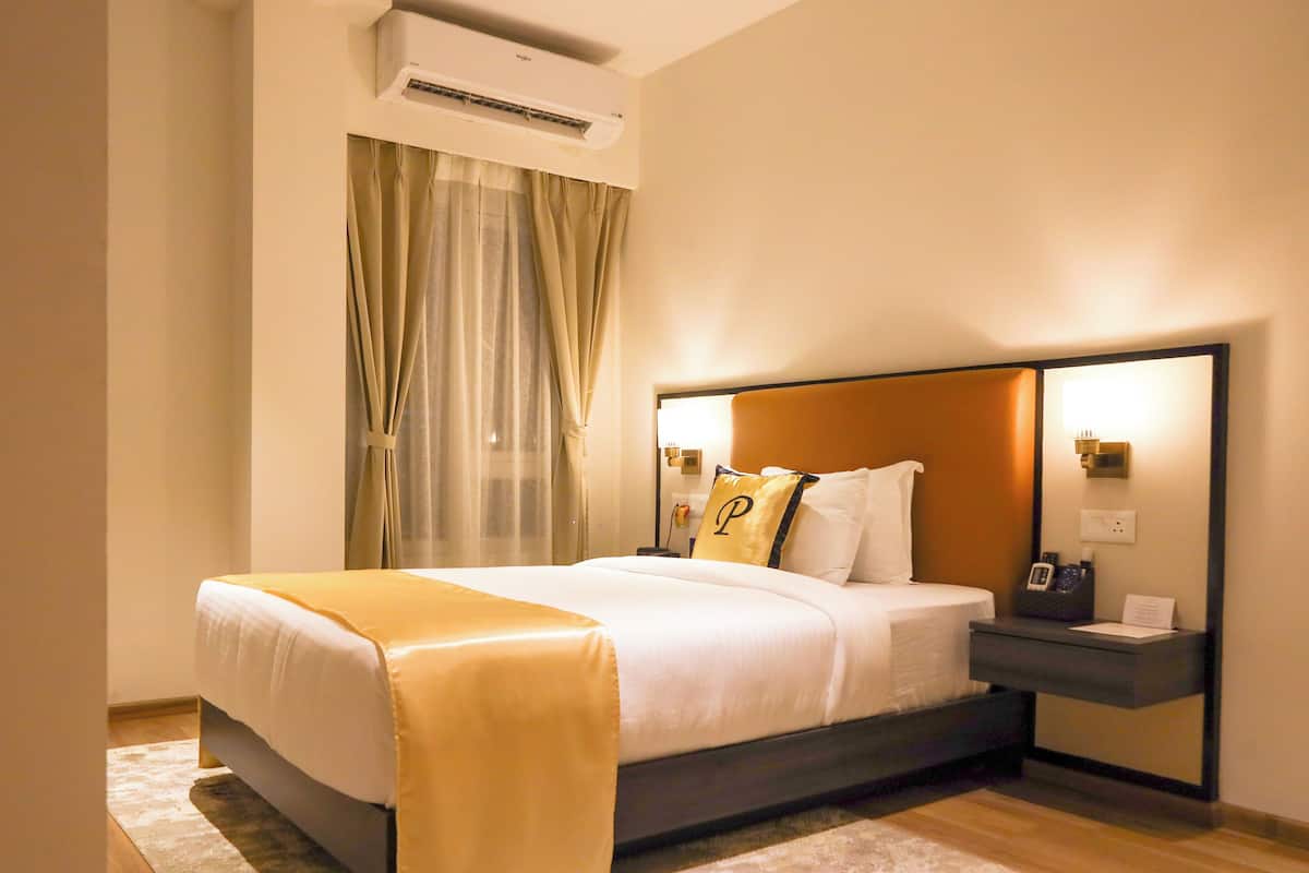 A hotel room with a bed, bedside table, lamp, and a window with curtains.