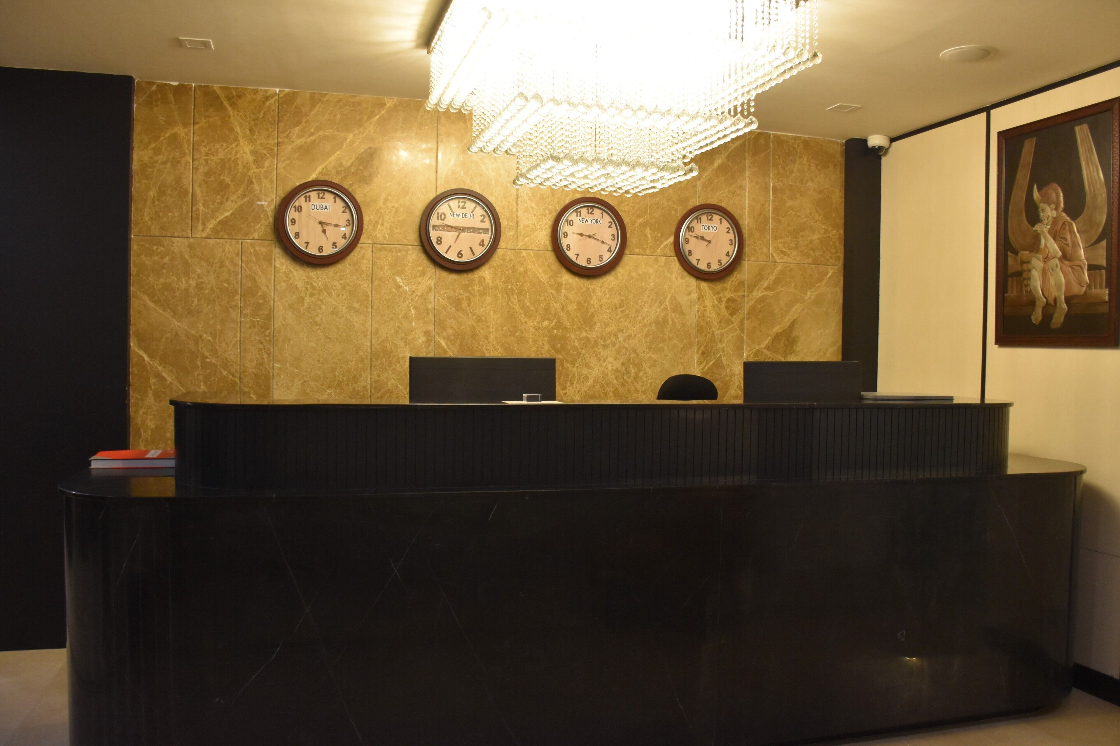 A reception desk with three clocks displaying different time zones, a chandelier, and a framed artwork on the wall.