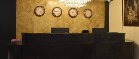 A reception desk with three clocks displaying different time zones, a chandelier, and a framed artwork on the wall.
