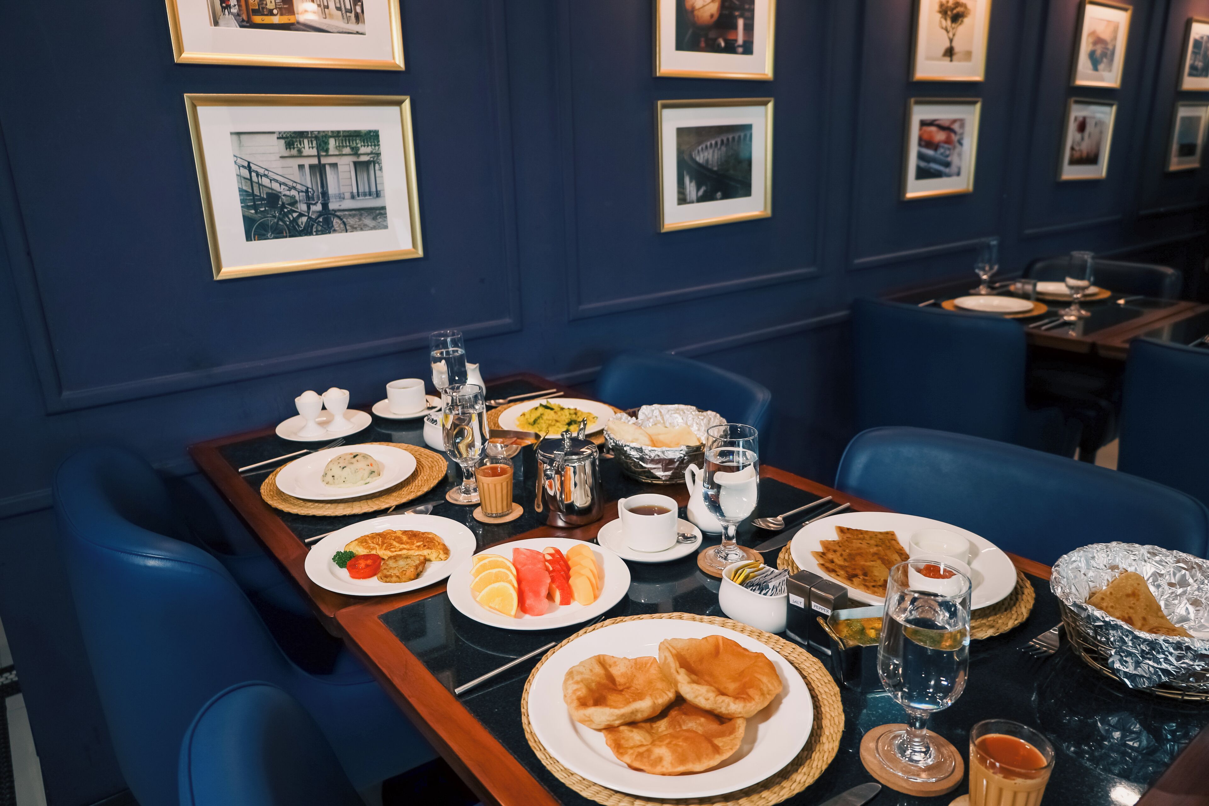 A dining table set with various dishes, glasses, and cutlery in a room with blue walls and framed pictures.