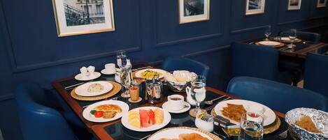 A dining table set with various dishes, glasses, and cutlery in a room with blue walls and framed pictures.