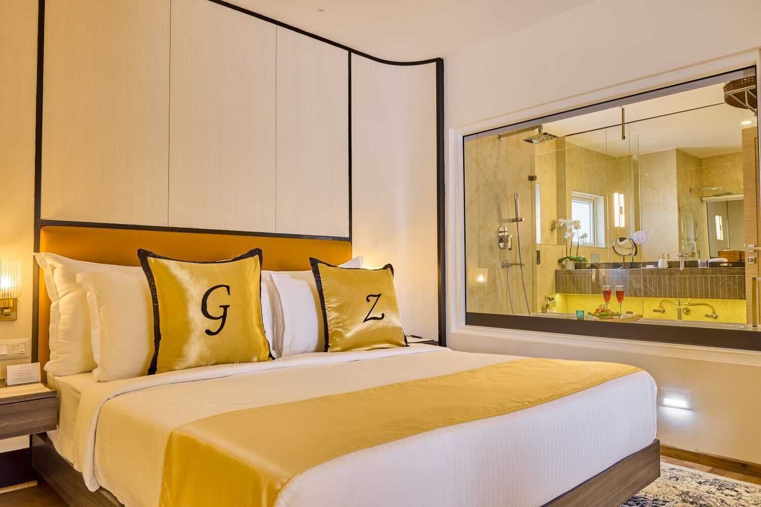 A hotel room with a large bed, a headboard with storage, a large mirror, and a view of the bathroom.