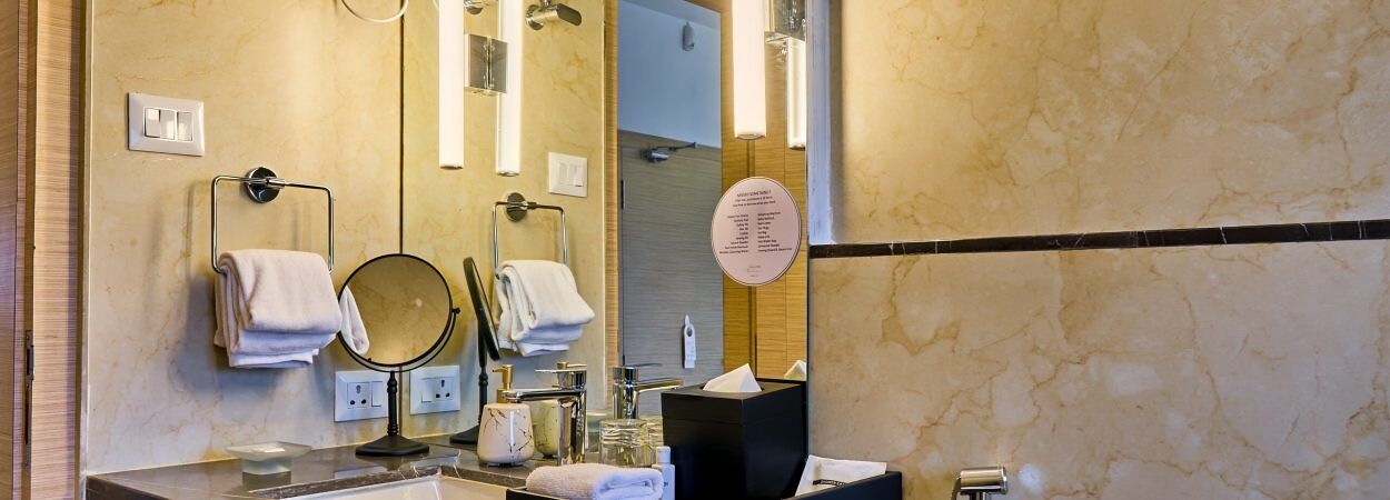 Une salle de bain moderne avec un comptoir en marbre, un miroir rond, deux porte-serviettes et un distributeur de savon noir.