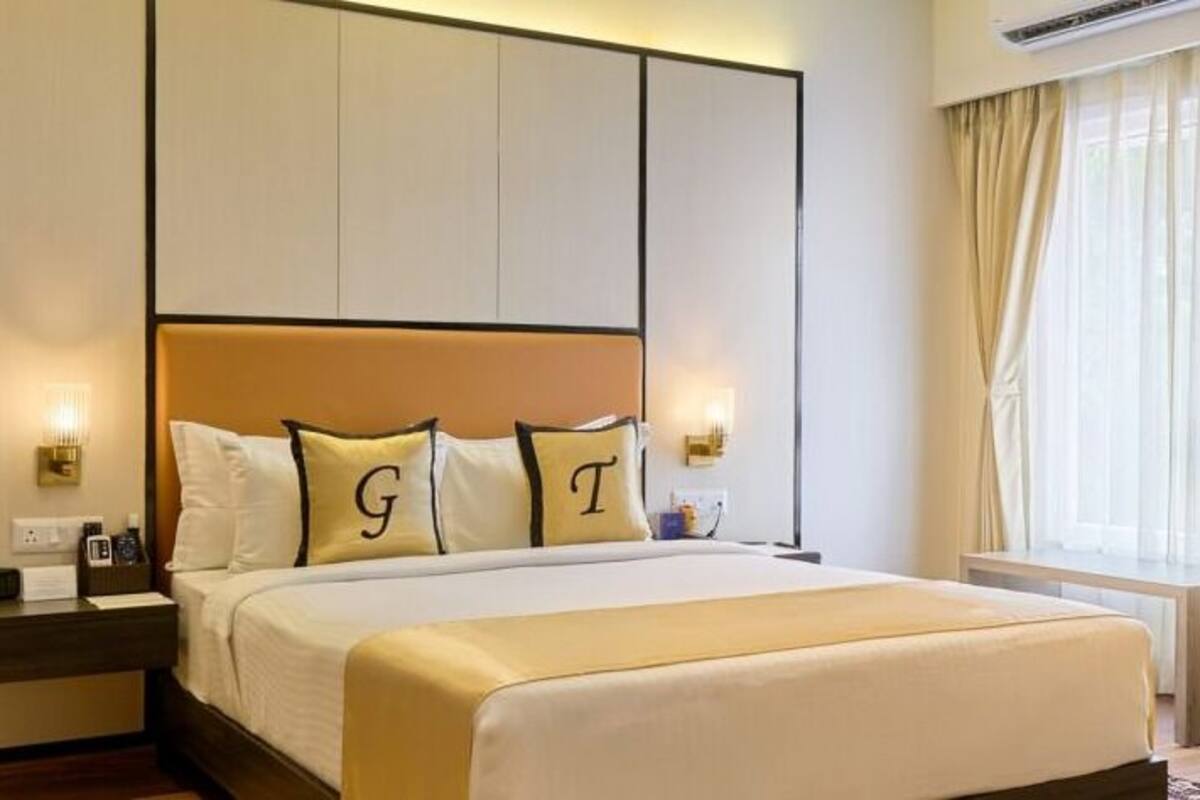 A hotel room with a large bed, a nightstand with a lamp, and a window with curtains.