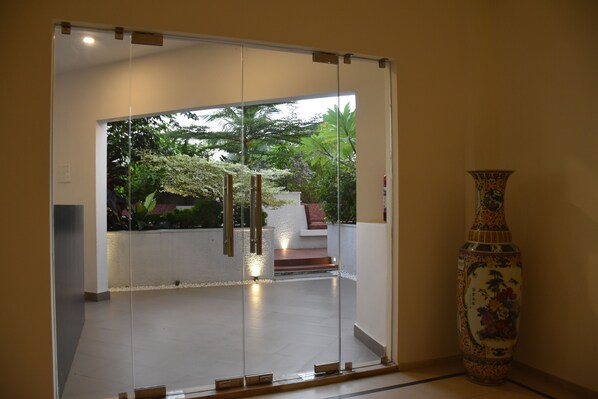 Un interior moderno con un vidrio que da a un jardín. Se observa un jarrón decorativo a la derecha.