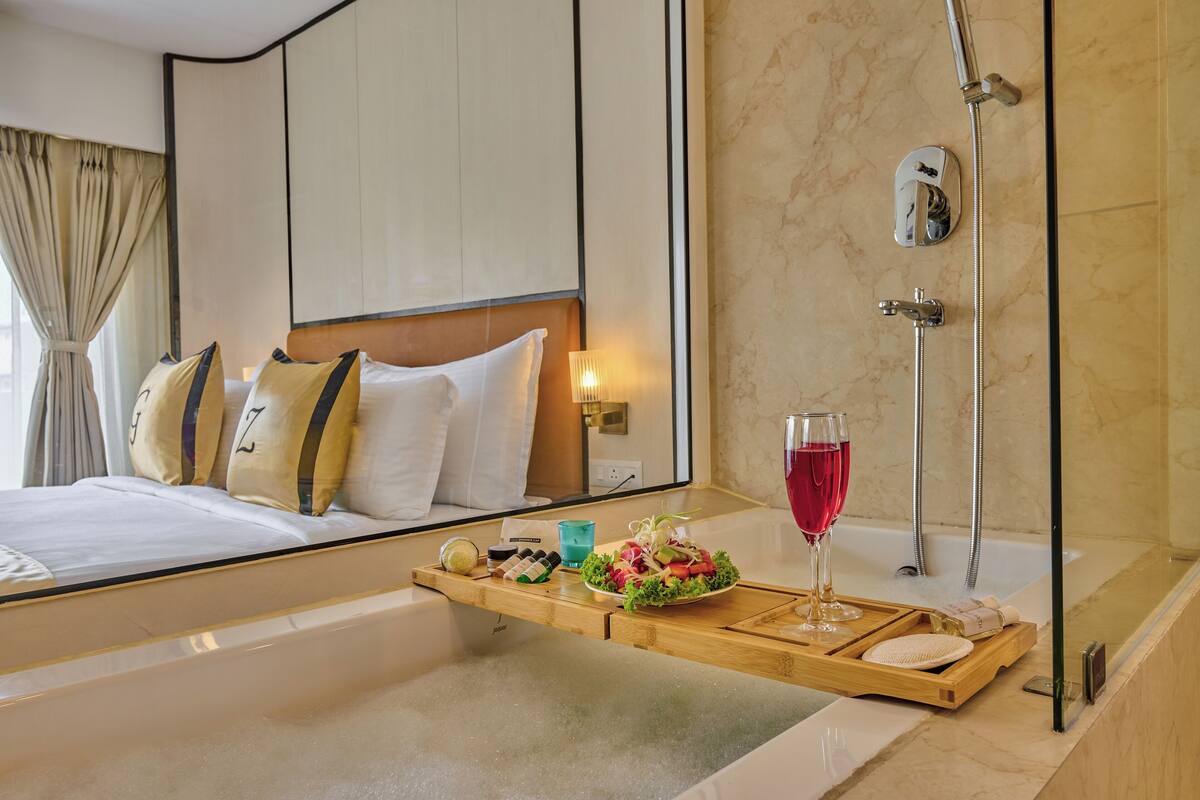 A hotel room with a bed, a bedside table with a tray of food and drink, a shower, and a large mirror.