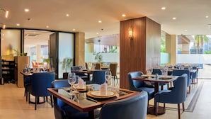 A modern restaurant with glass tables, blue chairs, and a view of greenery outside. - SHULEM BOUTIQUE HOTEL (Dimapur)