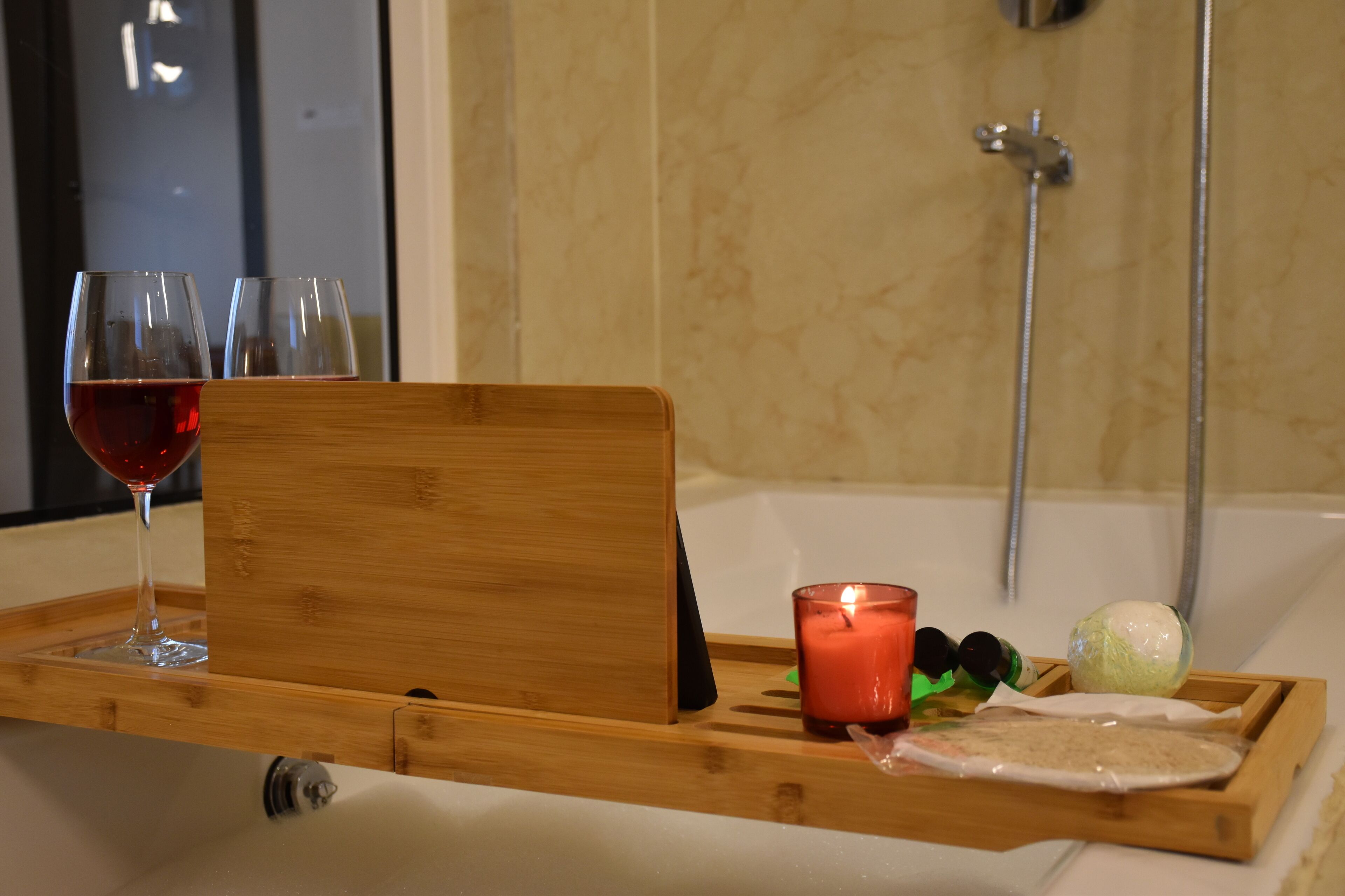 A wooden tray with a glass of red wine, a lit candle, and a towel on a bathroom counter.