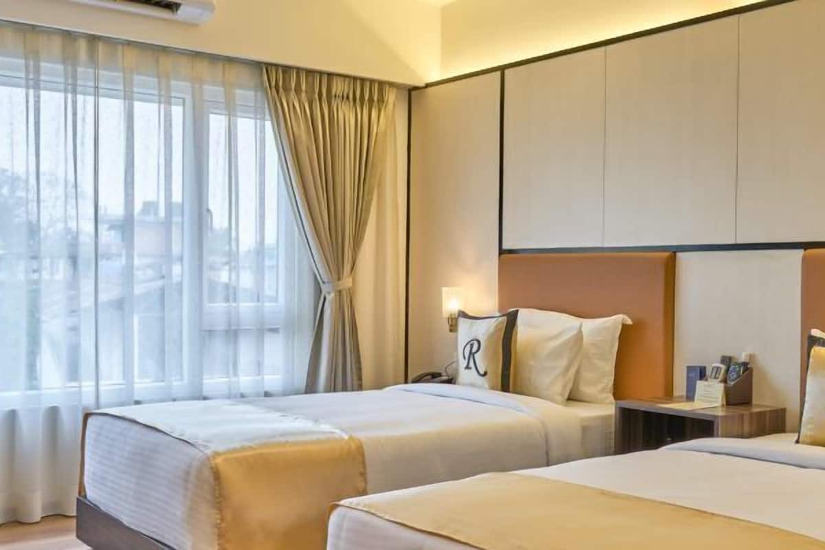 A hotel room with two beds, a large window with sheer curtains, and a city view.