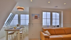 A modern living space with a dining area, a sofa, and large windows. - Beach Villa Marina 26 Sea View (Wangerooge)