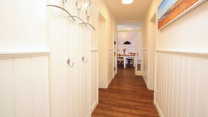 Un couloir aux murs recouverts de panneaux blancs, doté d’un plancher en bois et comprenant, au fond, un coin repas.