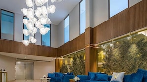 A spacious lobby with a blue sofa set, a modern chandelier, and a large window overlooking greenery. - Zavos Aqua Park Club Apt (Limassol)