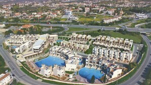 A residential area with modern apartment buildings, a central swimming pool, and a curved road. - Zavos Aqua Park Club Apt (Limassol)