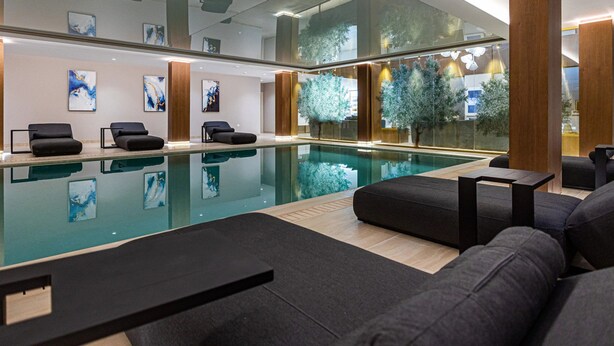 A modern indoor pool area with lounge seating and artwork on the walls. - Zavos Aqua Park Club Apt (Limassol)