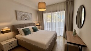 A hotel room with a bed, bedside tables, a desk, a mirror, and a window with curtains. - Zavos Aqua Park Club Apt (Limassol)