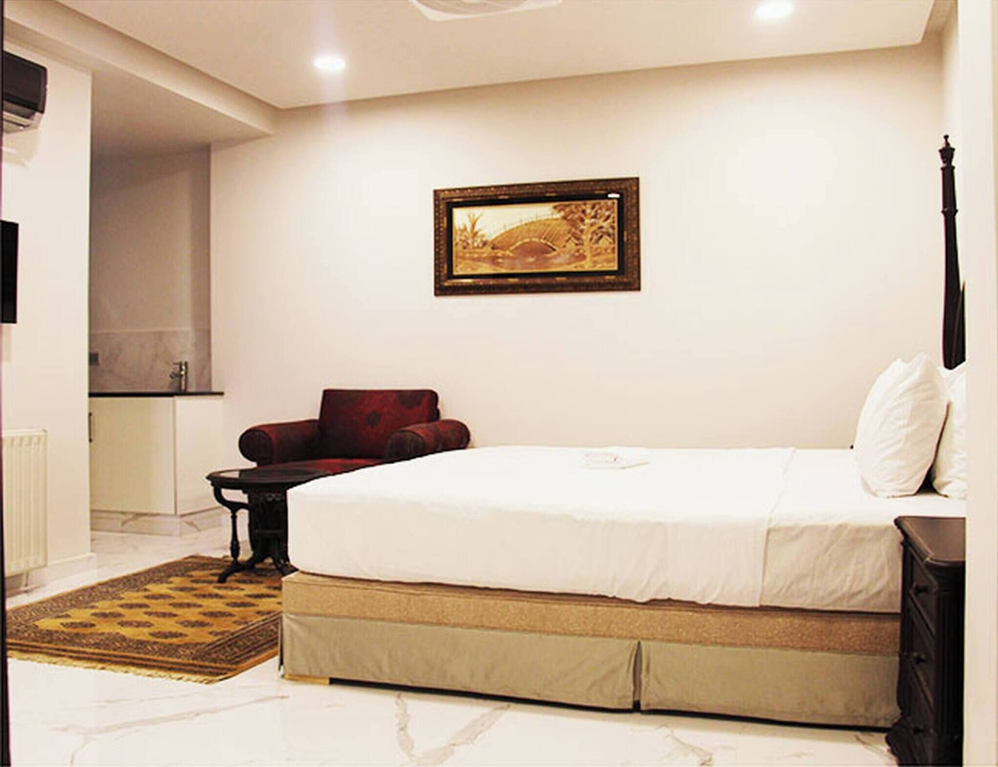 Une chambre avec un grand lit, une chaise, une petite table et un tableau accroché au mur.