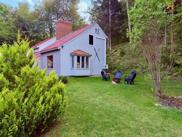 A small, single-story house with a red roof and a chimney, surrounded by a grassy yard and trees. - Holiday Haus- Fireplace, Game Room, NearTrails! (Killington)