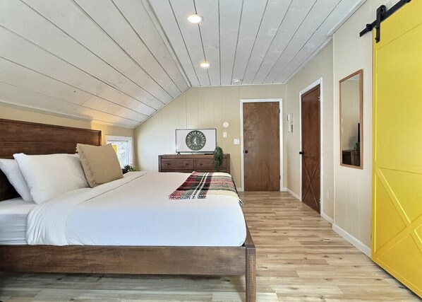 A bedroom with a wooden bed, a small bedside table, a clock, and a yellow door. - Holiday Haus- Fireplace, Game Room, NearTrails! (Killington)