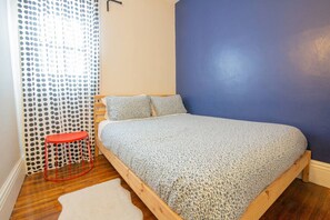 Une chambre à coucher avec un lit, un tabouret rouge, un tapis blanc et un rideau à pois.