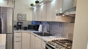 Una cocina moderna con armarios blancos, electrodomésticos de acero inoxidable, estufa a gas y un letrero que dice 'cafetería'.